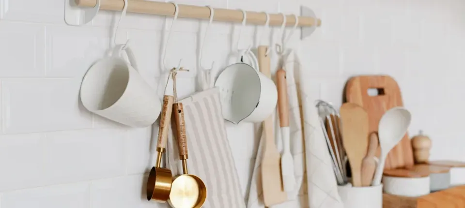 hooks on a wall holding kitchen utensils, mugs and dishtowels